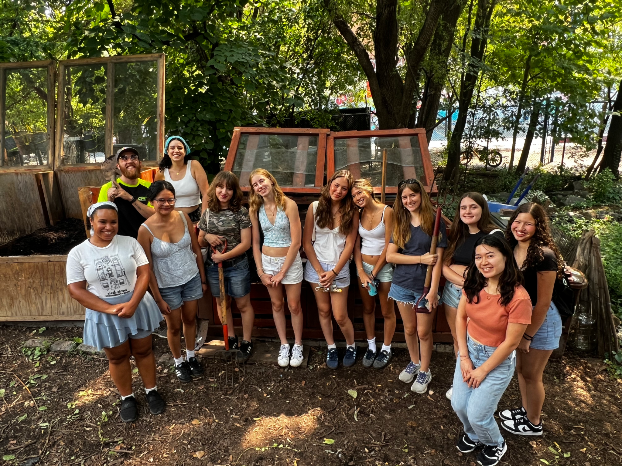 A group of young people pose for a photo outdoors in front of an wooden compost bins.