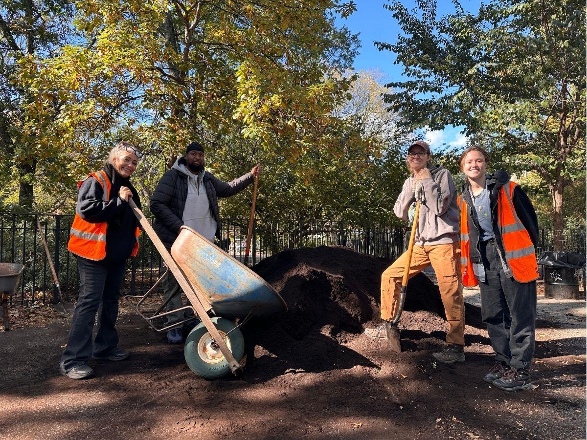 People standing in front of a compost pile with wheelbarrows and shovels.